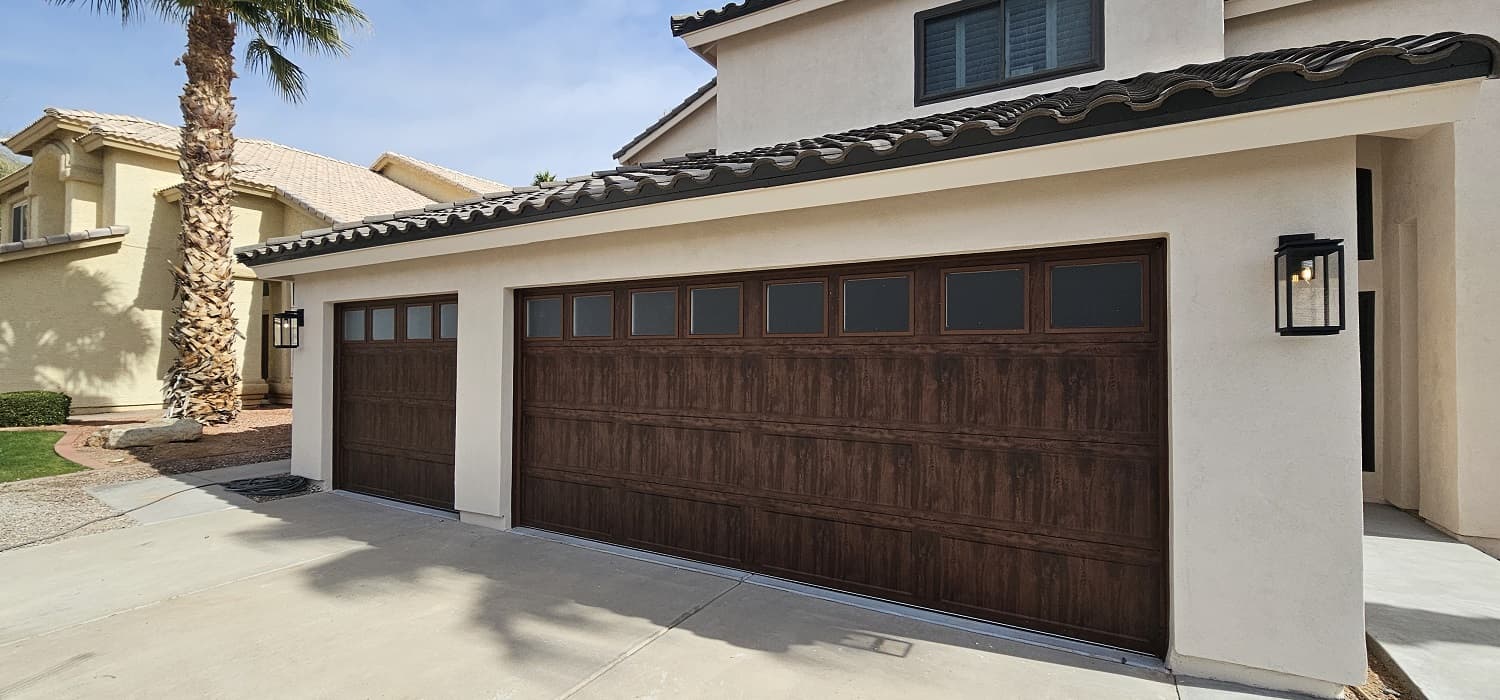 Two-story Arizona stucco home with dark wood-look carriage garage doors under a clear blue sky